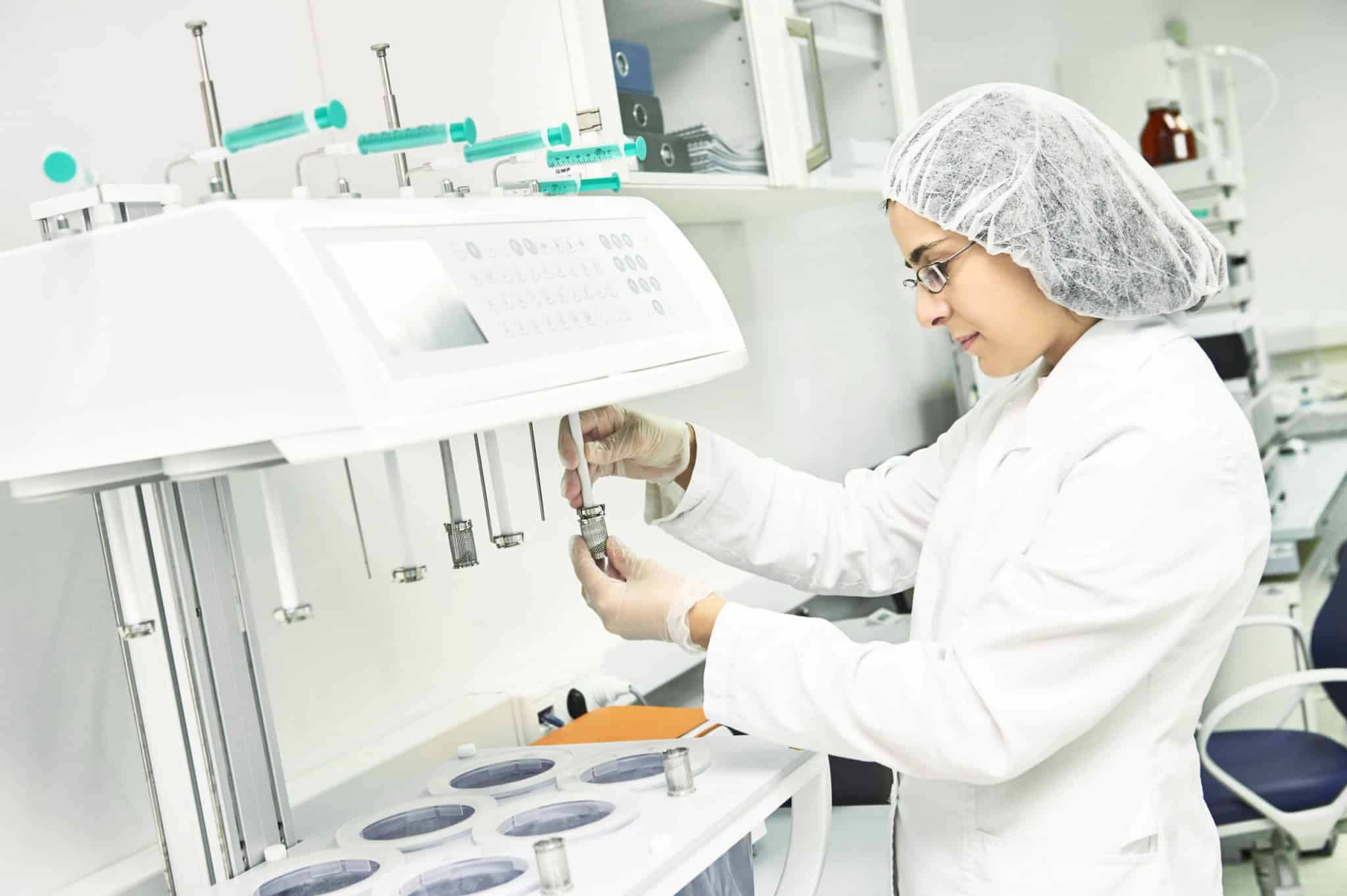 woman dressed in white lab coat and protective hairnet putting medication into a tube at a compounding pharmacy