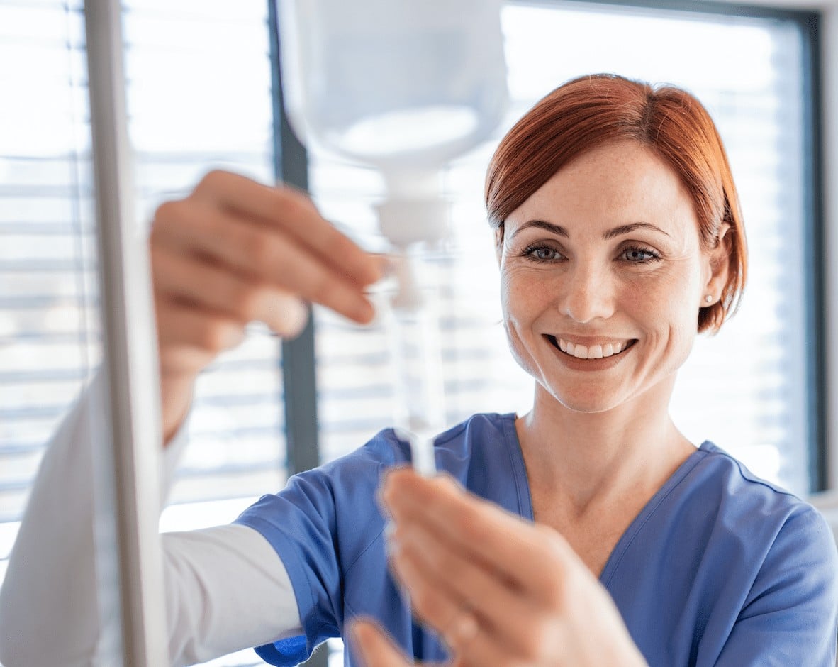 Female Nurse Smiling While Adjusting IV Nutritional Therapy Drip.