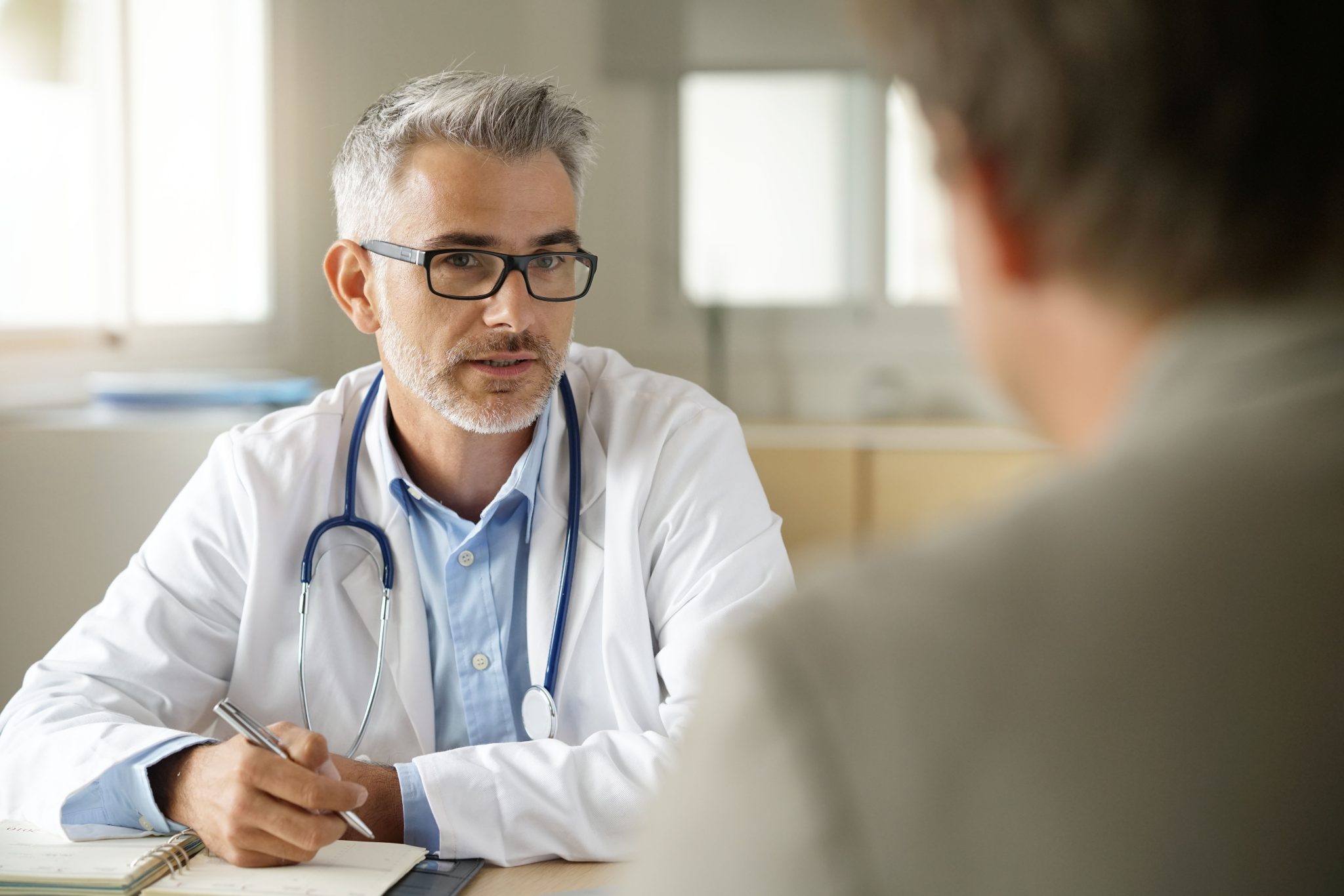 A healthcare professional with a stethoscope around his neck, engaged in a conversation with a patient.