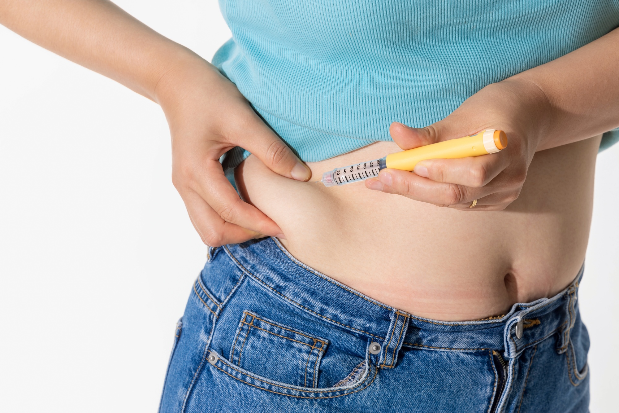 A person wearing jeans is using an injection pen on their abdomen.