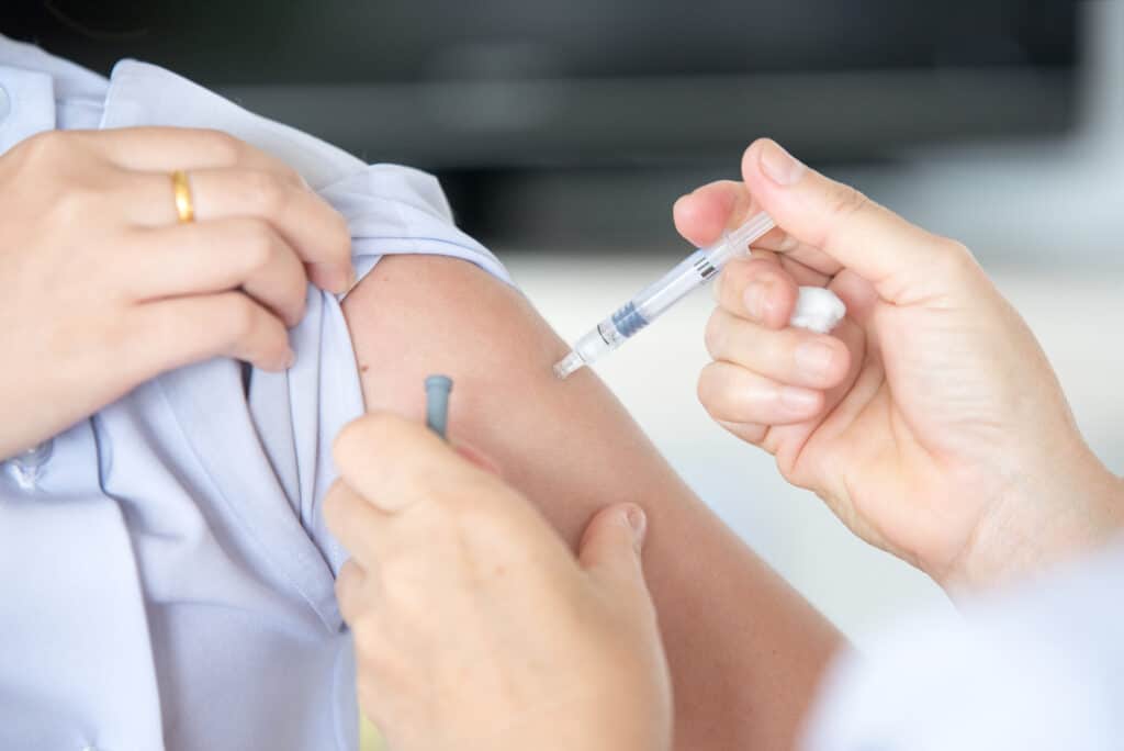 A close-up of a patient receiving an intramuscular injection in the upper arm, administered by a healthcare worker.