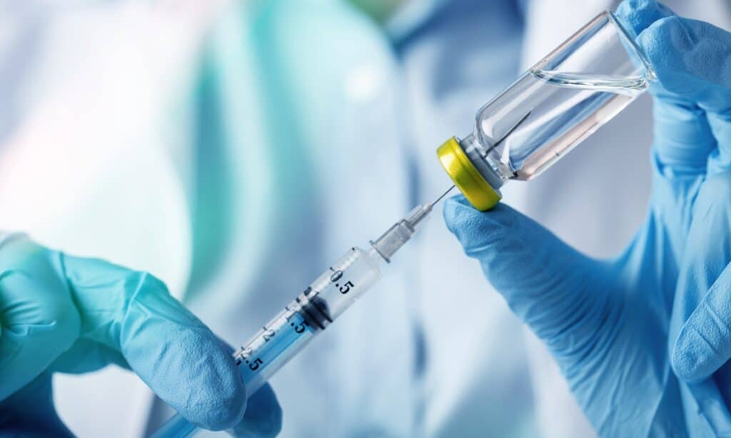 A gloved healthcare professional drawing a clear liquid medication from a vial into a syringe.